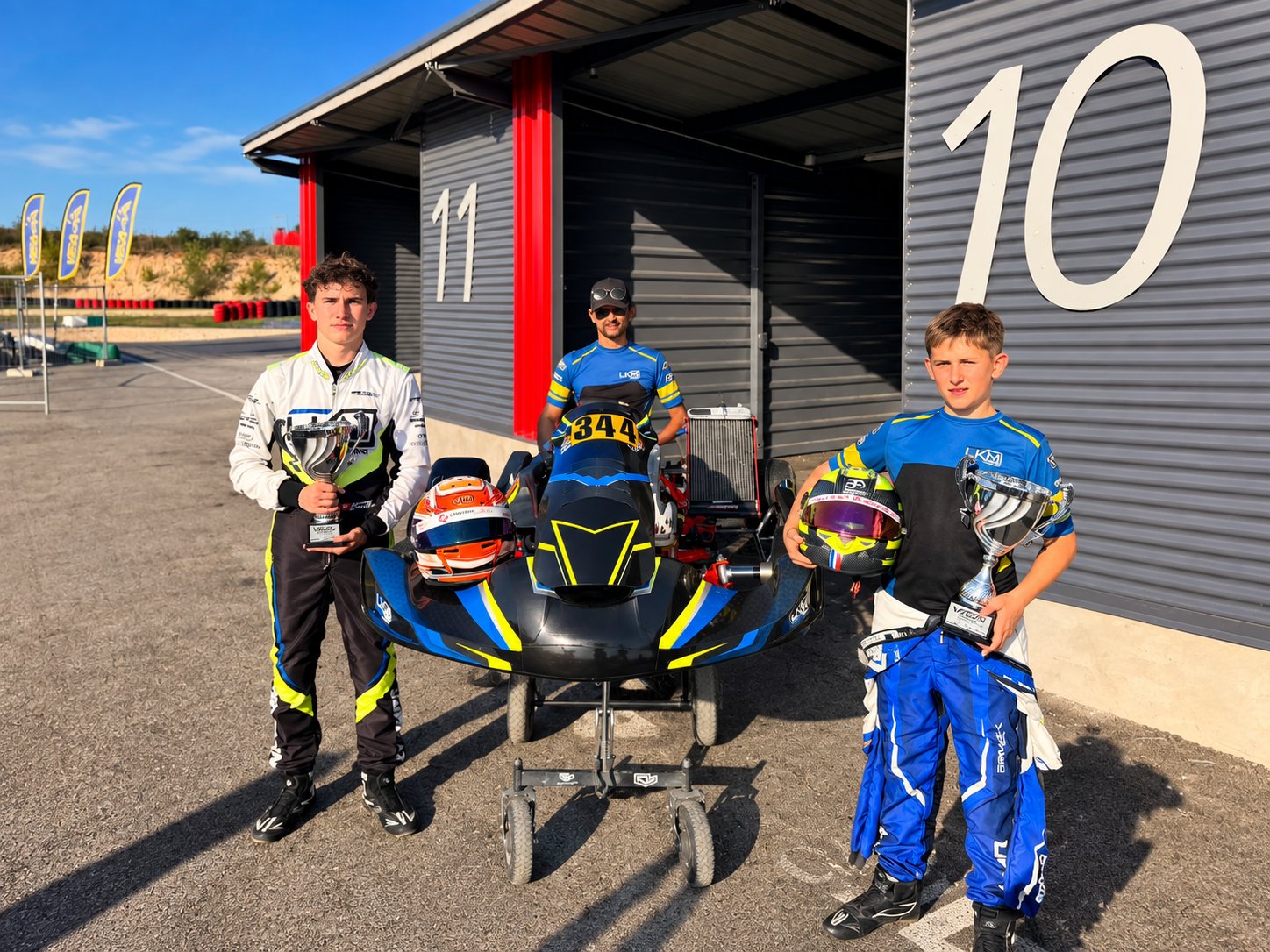 Deux pilotes LKM Racing avec leurs trophées devant le kart au coucher de soleil
